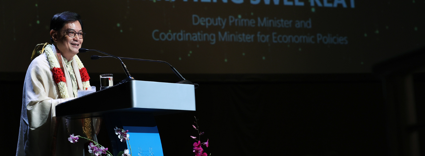 Heng Swee Keat speaks at podium; text reads "Deputy Prime Minister," flower garland around neck.
